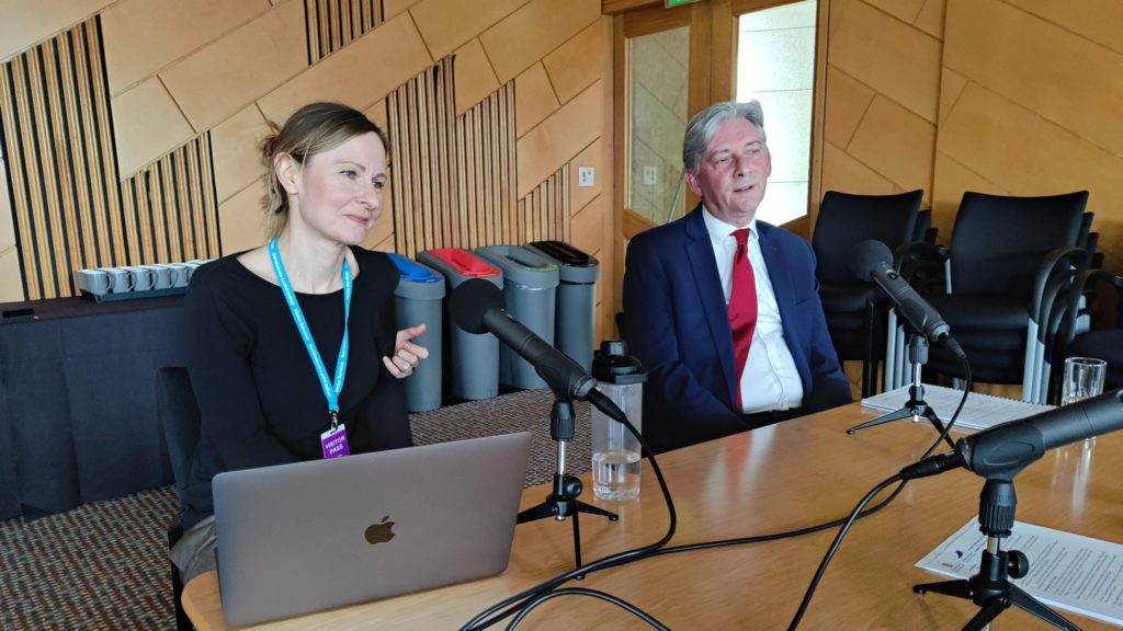 Two people sitting at a table with a microphone in front of them